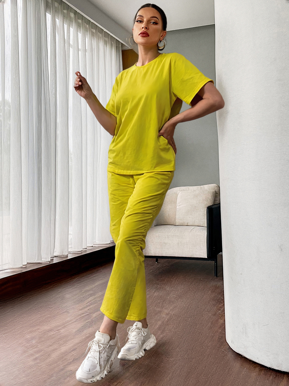 Woman in a bright yellow outfit standing in a modern room with white curtains and a gray wall.