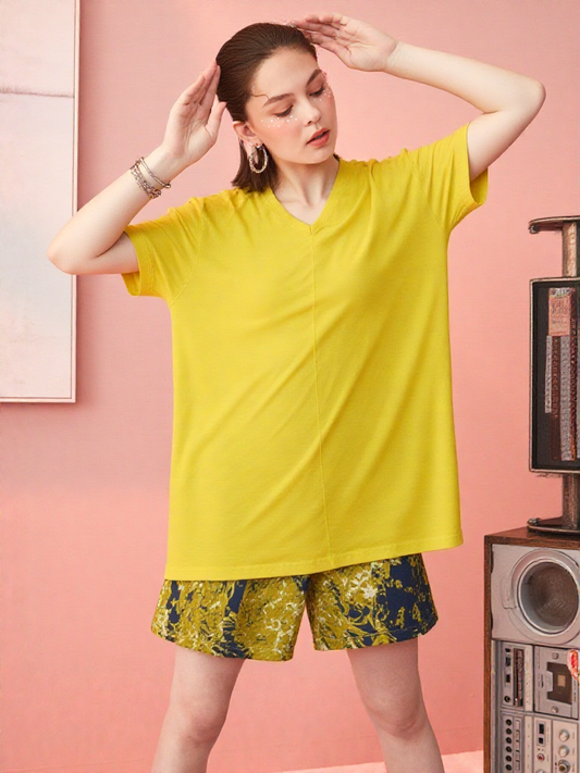 Woman wearing a yellow oversized t-shirt and patterned shorts against a pink background
